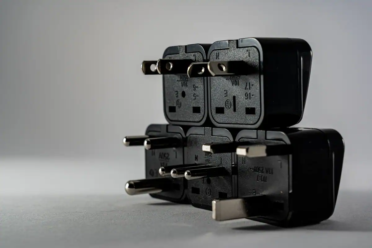 Mai multe adaptoare negre de priză suprapuse, cu ștecheruri de tipuri diferite pentru călătorii