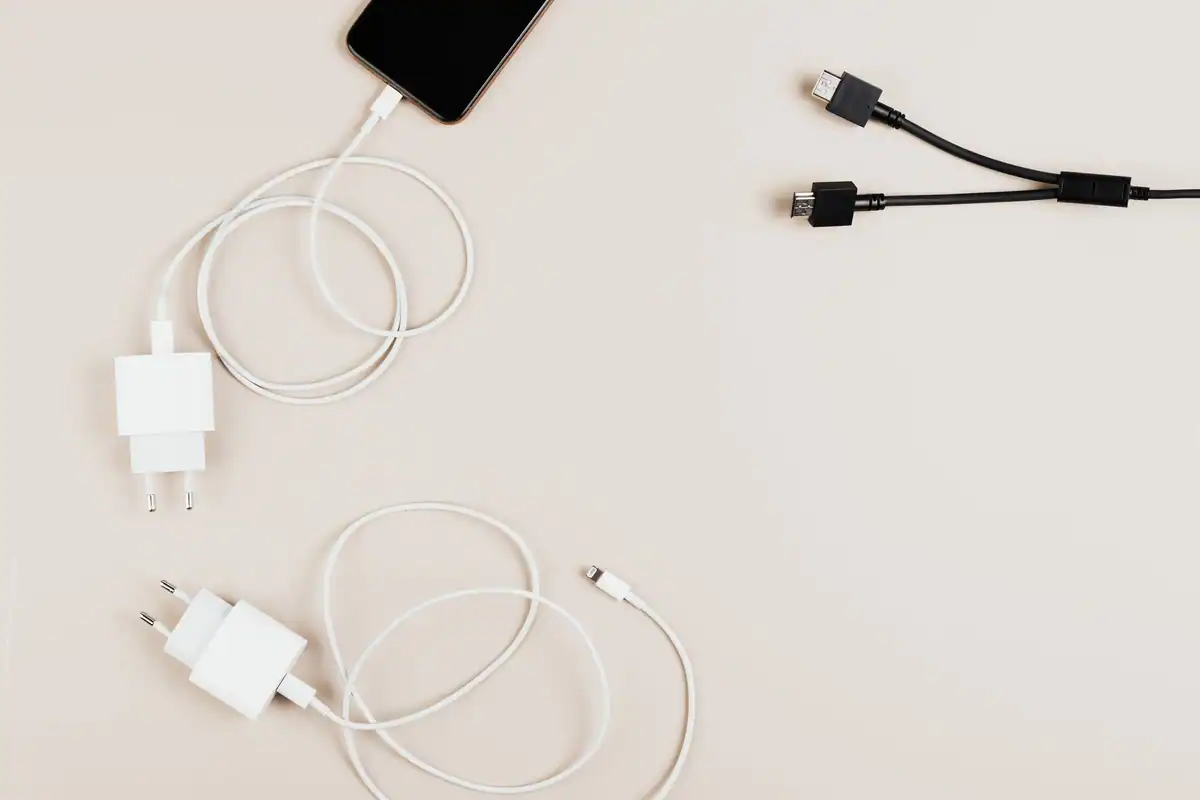 Încărcătoare albe și cabluri USB așezate pe o masă lângă un telefon conectat