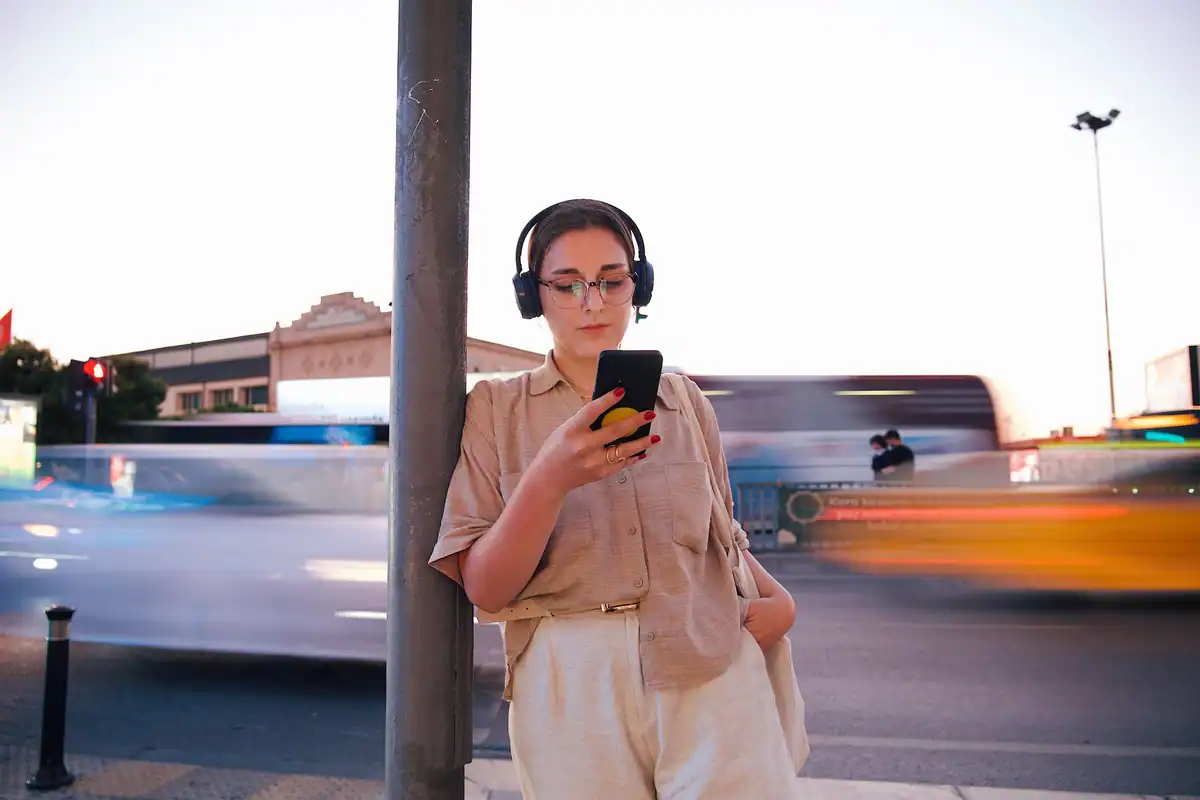 Tânără cu căști pe urechi, care folosește telefonul pe o stradă aglomerată