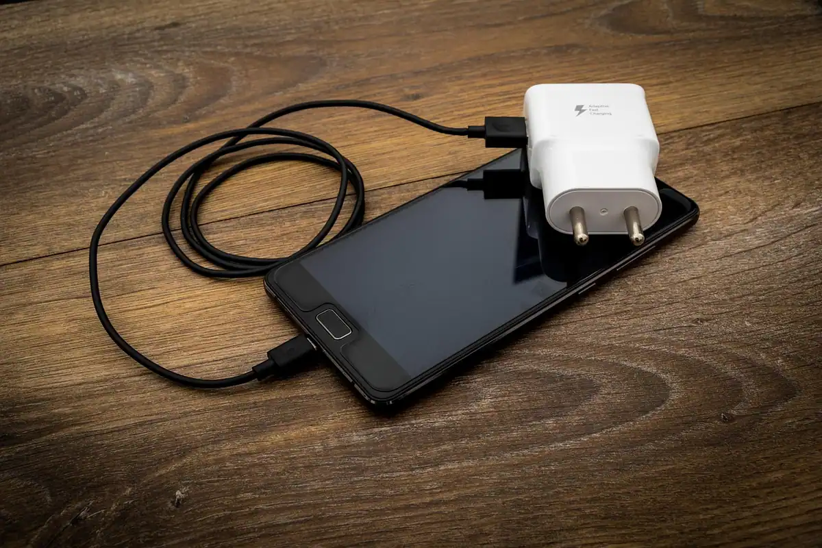 Cablu USB și adaptor de priză așezate pe o masă, folosite pentru încărcarea căștilor wireless