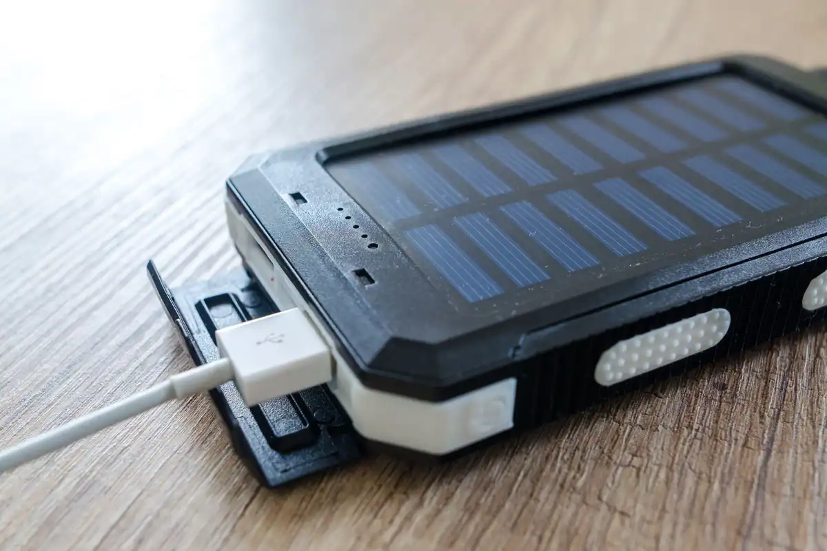 Baterie externă solară, rezistentă, conectată la un cablu USB pe o masă de lemn