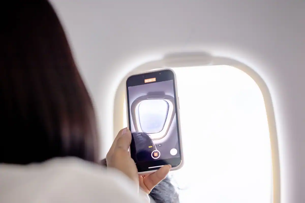 Pasager care fotografiază cu telefonul pe geamul unui avion, în timpul zborului