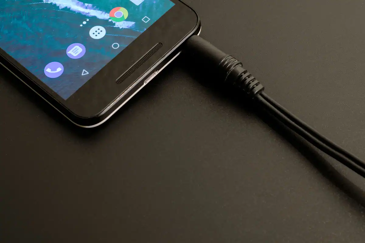 Telefon încărcat cu un cablu negru, văzut de aproape pe o masă întunecată