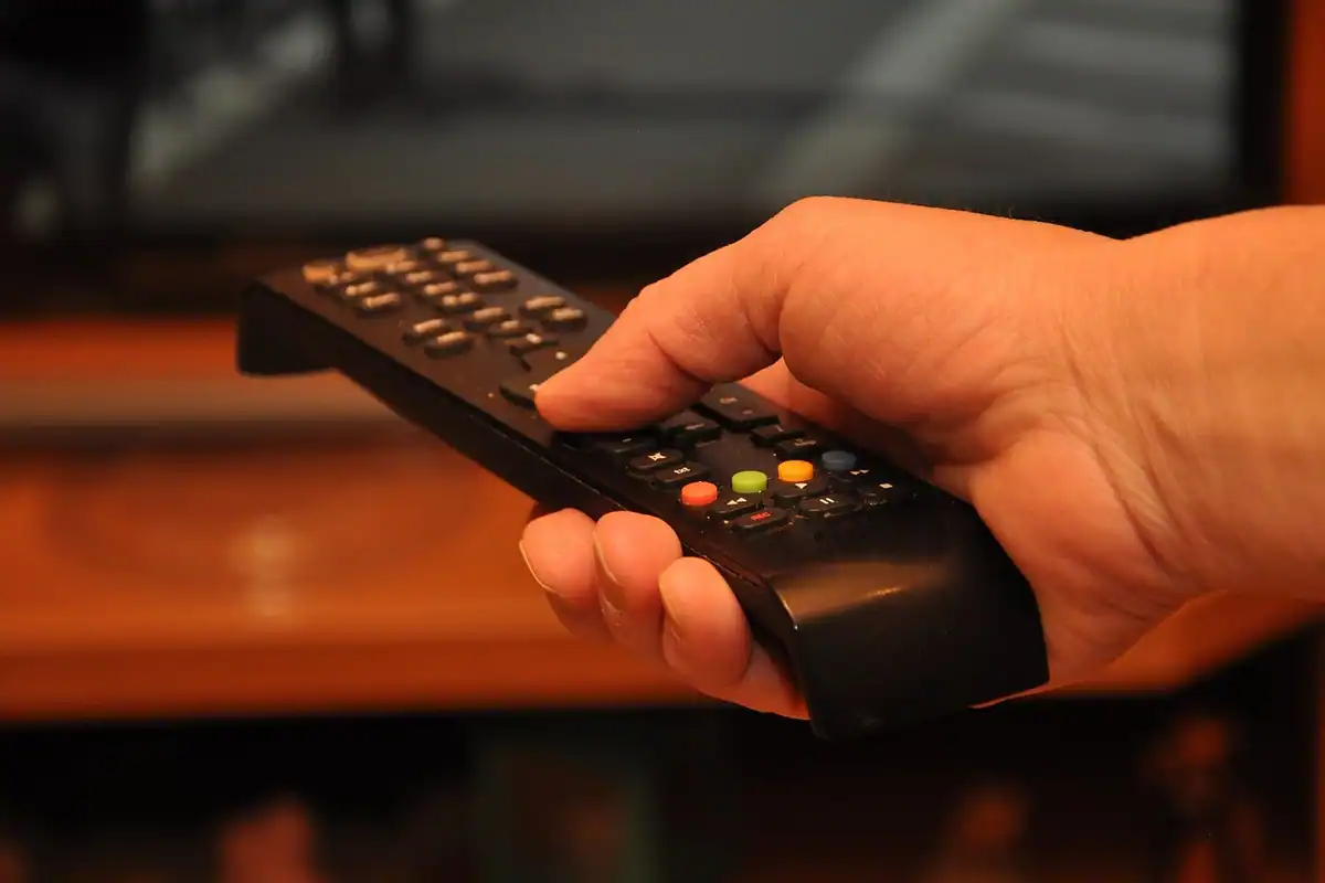 Mână care ține o telecomandă neagră de televizor, un aparat alimentat cu baterii
