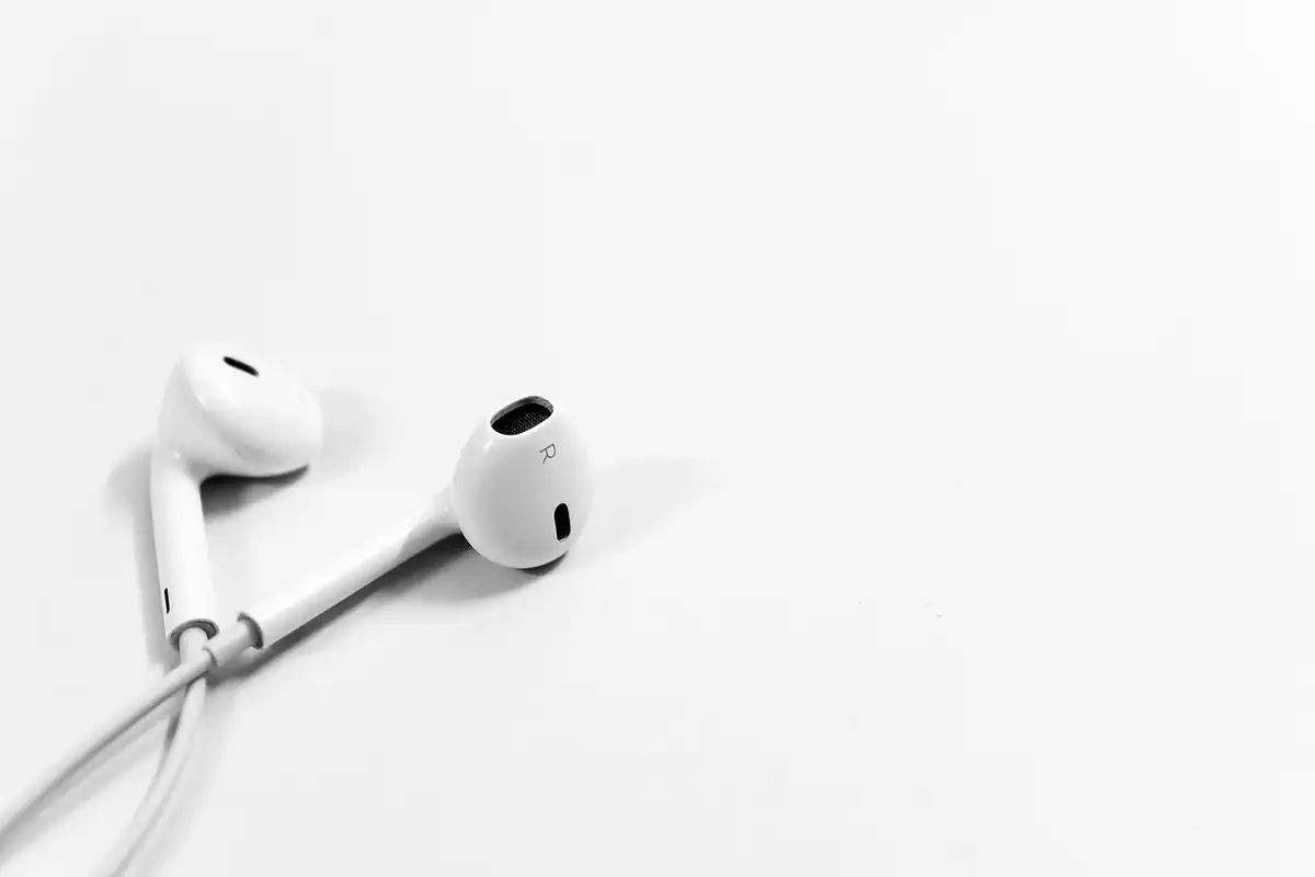 Două căști intra-auriculare albe, cu fir, așezate pe un fundal alb