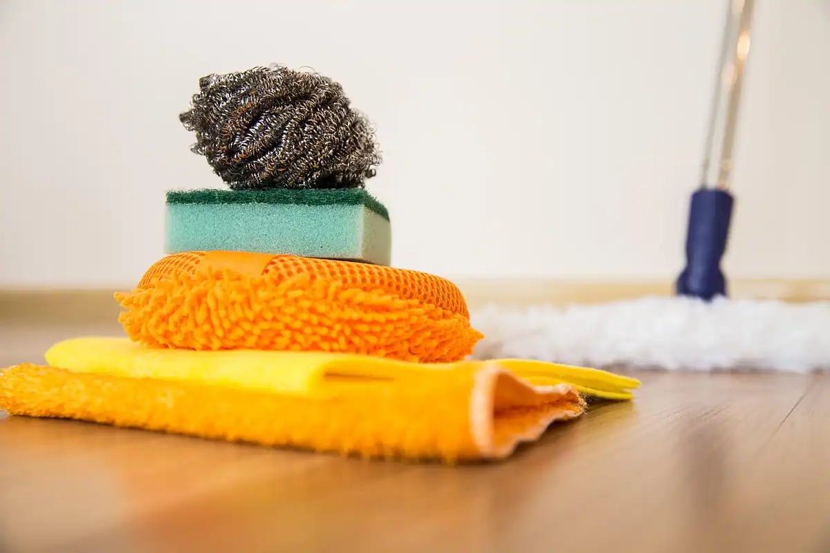 Bureți și cârpe colorate pentru curățenie, lângă un mop, pe un parchet