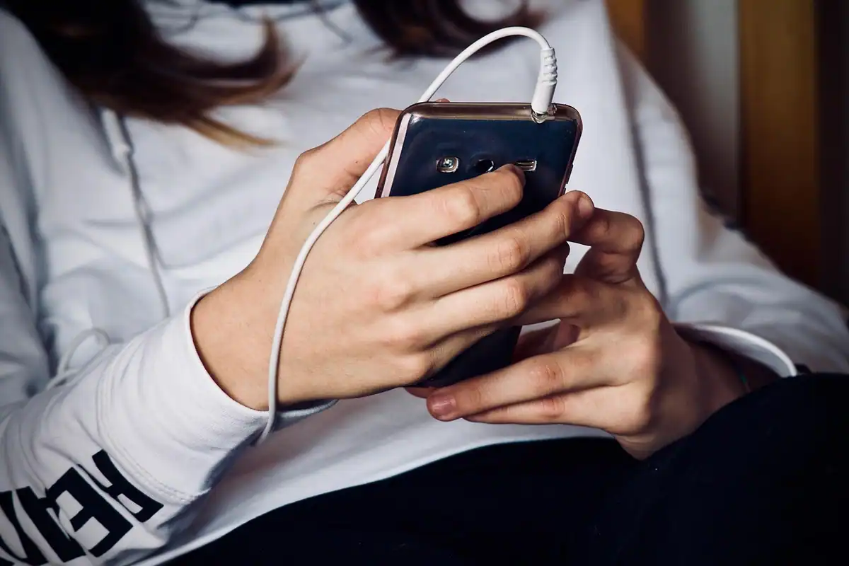 Fată care ține un telefon conectat la căști cu fir, îmbrăcată într-o bluză gri