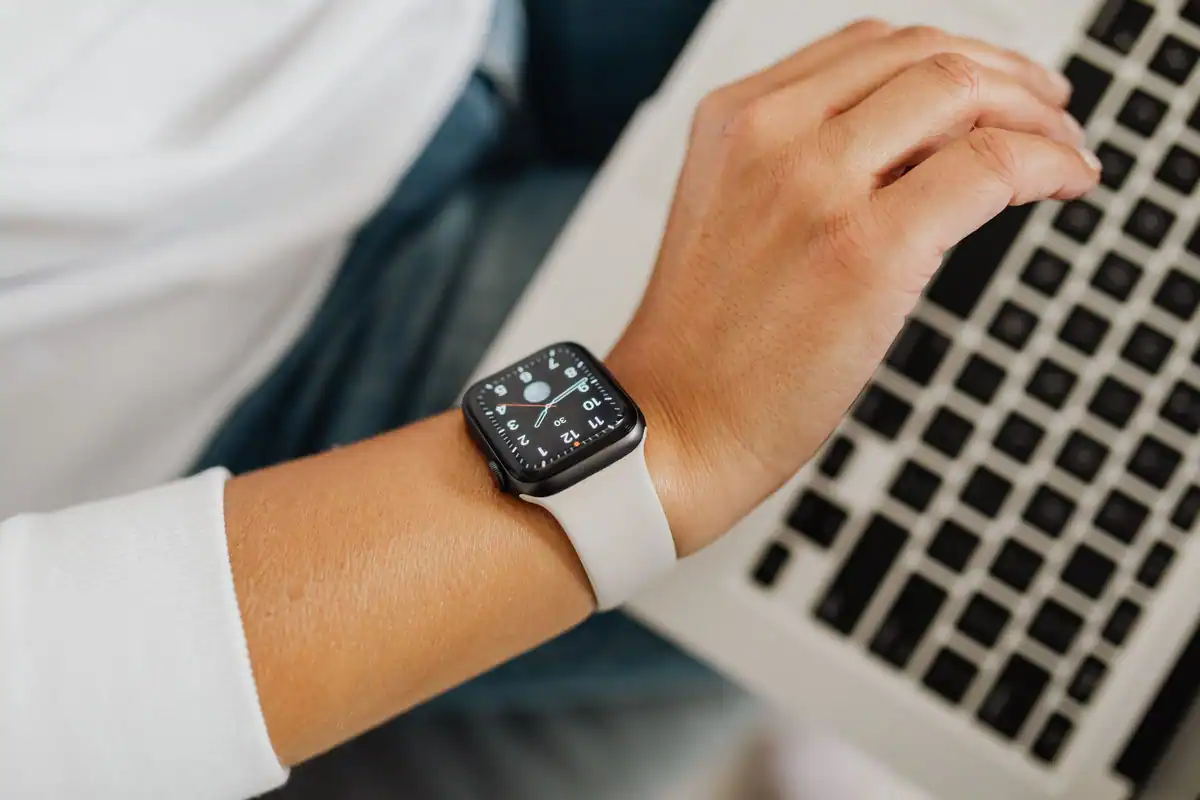 Persoană cu un smartwatch la mână lucrează la laptop