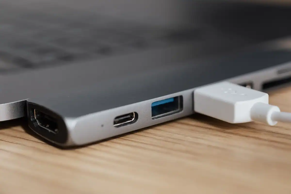 Adaptor USB-C cu mai multe porturi, conectat printr-un cablu alb la un laptop modern