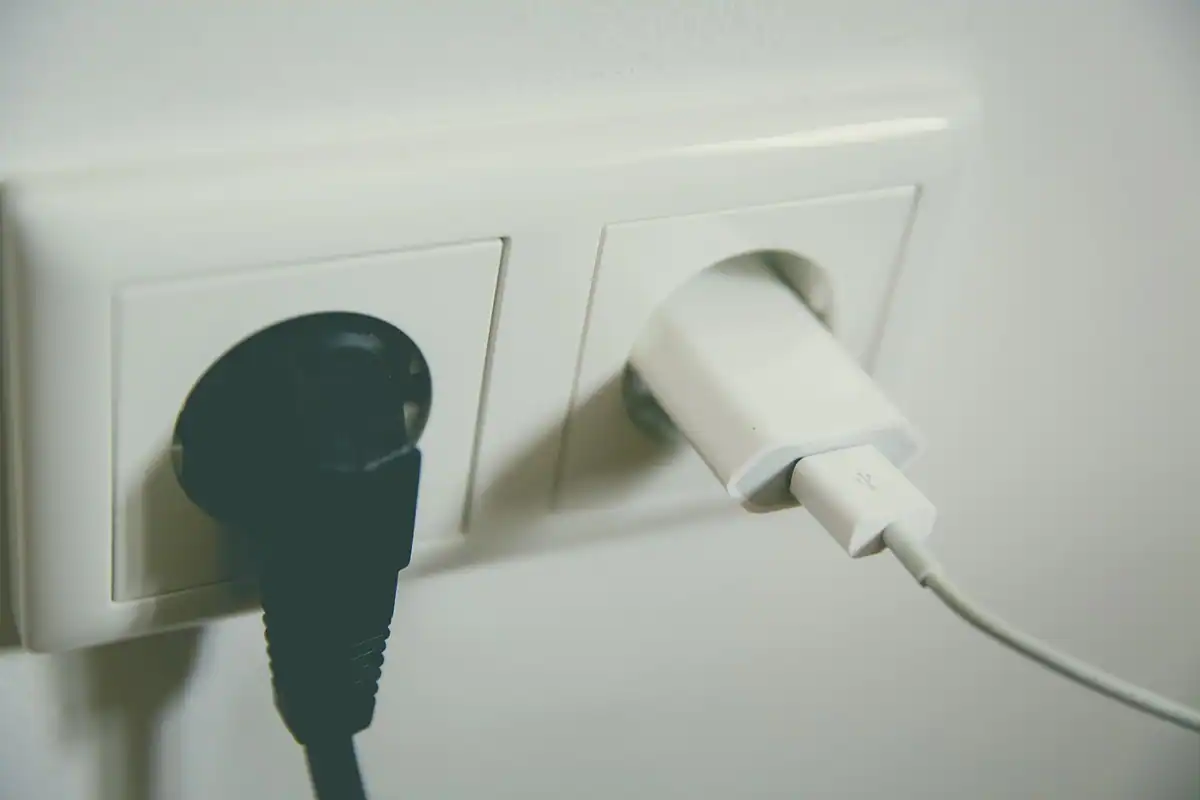 Ștecher electric și cablu USB văzute de aproape, lângă o priză de curent