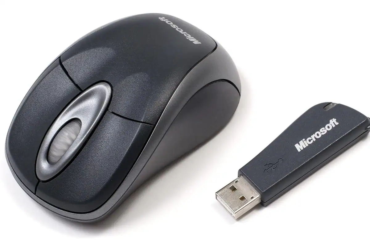 Receptor USB mic așezat lângă un mouse wireless, pe o suprafață de birou