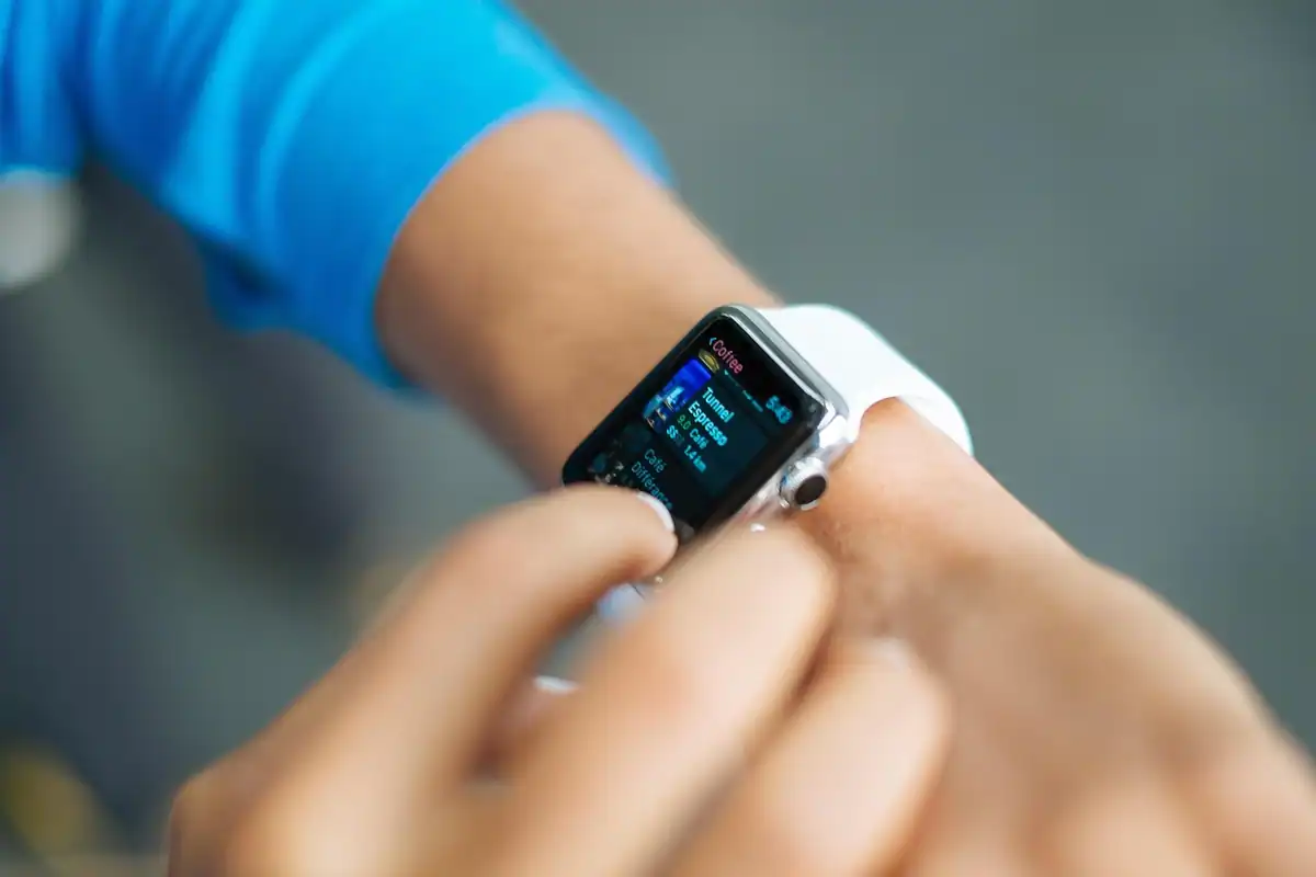 Persoană care atinge ecranul unui smartwatch cu curea albă, purtat la încheietura mâinii