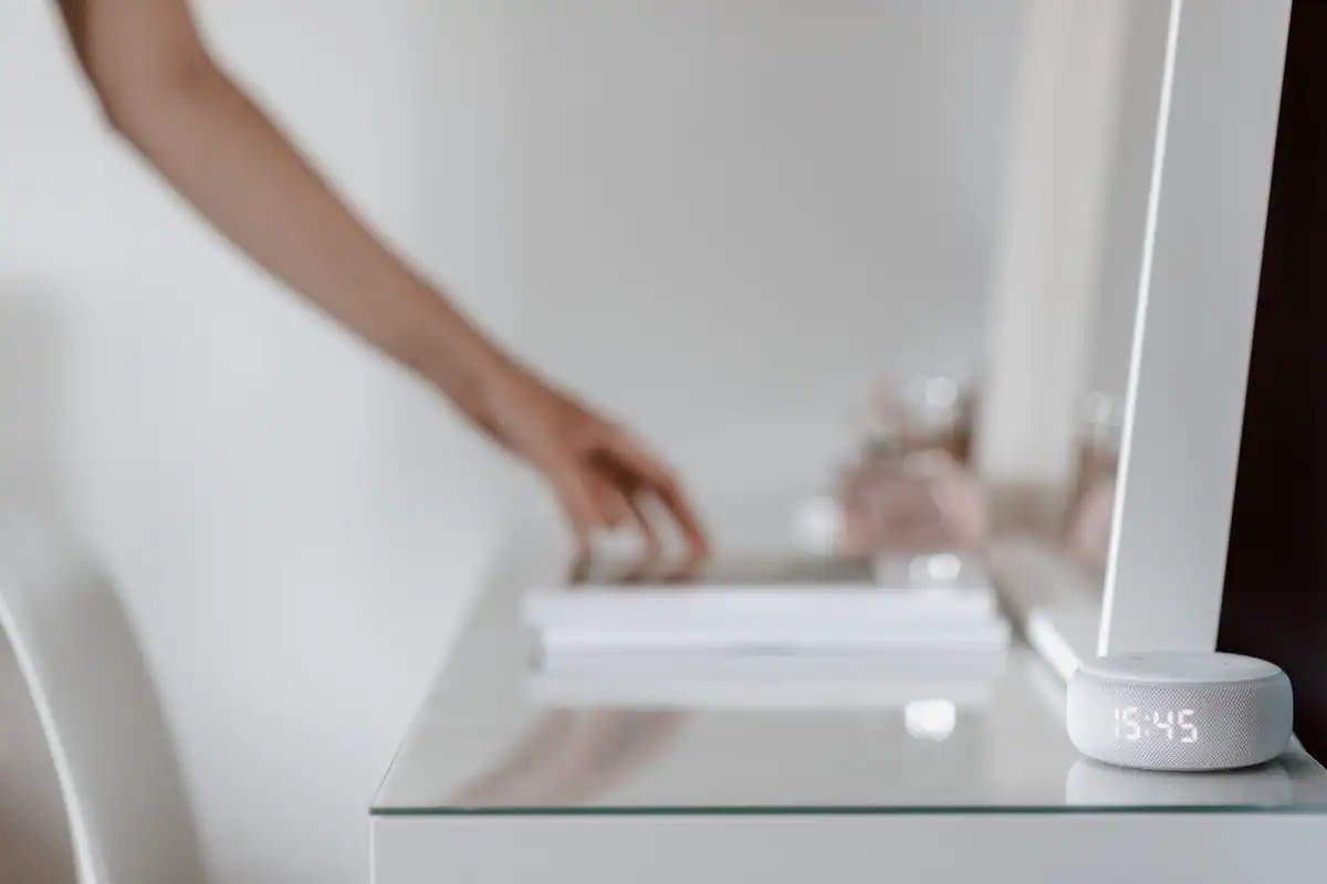 Mână care atinge un dispozitiv mic cu ceas digital, așezat pe o masă de sticlă