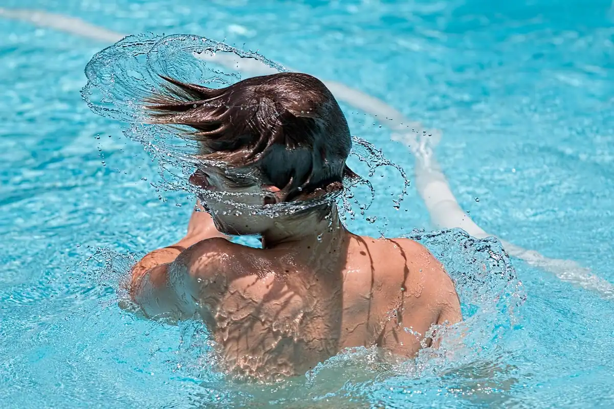 Persoană care înoată într-o piscină cu apă albastră, cu părul ud și stropi în jur