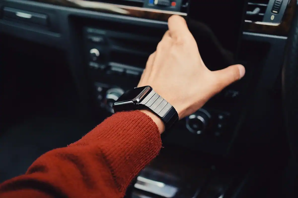 Mână cu un smartwatch, întinsă spre bordul unei mașini