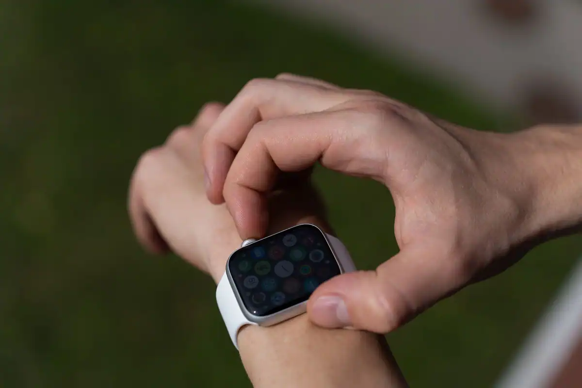 Persoană care atinge ecranul unui smartwatch cu curea albă, în aer liber