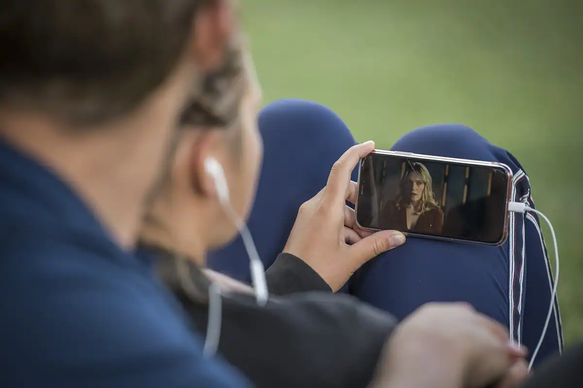 Persoană cu căști intra-auriculare care urmărește un film pe telefon, afară, în parc